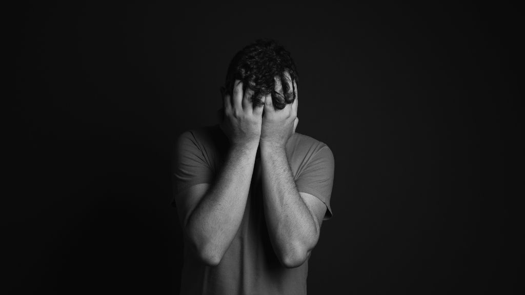 Man with Head in Hands on Black Background