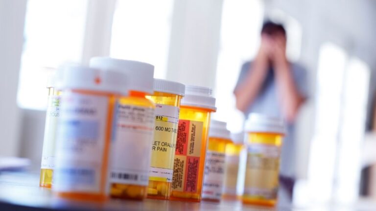 Table with Many Pill Bottles and Patient in Background with Head in Hands
